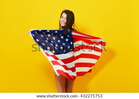 Beautiful patriotic young woman with the American flag held in her outstretched hands over bright yellow background. 4th july Independence Day concept
