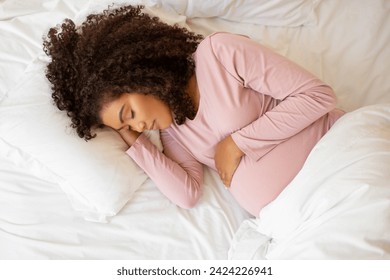 Beautiful peaceful black pregnant woman resting on white bed at home, calm african american expectant mother cradling her belly, depicting serene and tender moment in pregnancy, above shot - Powered by Shutterstock