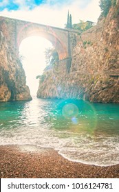 Beautiful Pebble Beach Overlooking Old Bridge At Sunset With Sun Shining Through At Fiordo Di Furore, Amalfi Coast, Italy