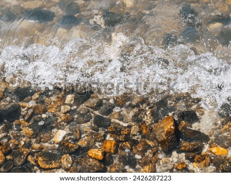 Beautiful pebbles on the beach close up. Water stones coast rocky. A close-up view of a beach with rocks and water. Wave Splashing On Rock.