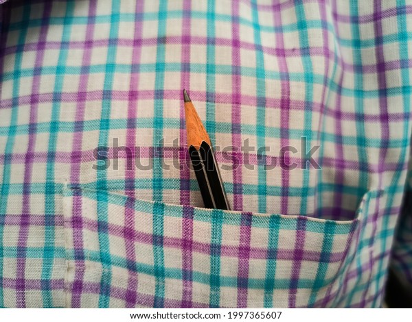 A beautiful pencil in the front pocket of shirt. Pencil\
is black in colour and the shirt colour is common in india. The\
line on the shirt are dividing each other and make a very beautiful\
pattern. 