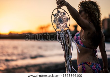 Beautiful people woman with bikini holding a white dreamcatcher outdoor at the beach enjoying sunset in a summer holiday vacation freedom feeling