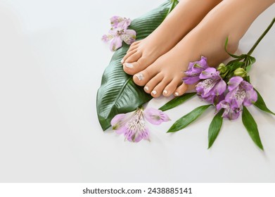 Beautiful perfect female skin legs feet top view with tropical flowers and green palm leaf. Nail polish, care and clean, spa pedicure treatment in white. Concept on a white background. Copy space - Powered by Shutterstock