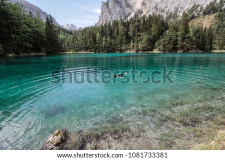Beautiful photo of girl floating in the Grunner See, or the Green Lake in Styria, Austria. Beautiful landscape with emerald green water, coniferous forest entouring the lake. Warm summer day. 