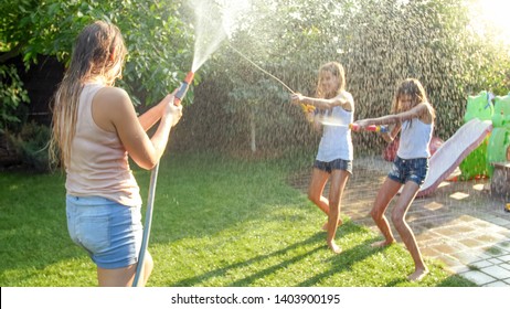 Beautiful Photo Of Happy Laughing Family With Children Having Fun At Hot Summer Day With Water Guns And Garden Hose. Family Playing And Having Fun Outdoors At Summer