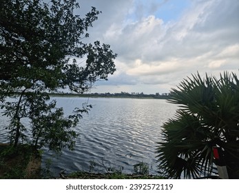 beautiful photograph of lakeside view palm bushes trees river Bank turquoise blue water cloudy day greenery fertile dam reservoir pond south india tamilnadu tourism wallpaper negative empty space 