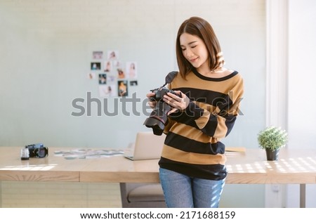Beautiful photographer Asian woman holding dslr camera in home office. Korean or Japanese female photographer standing in front of her workplace. Startup small business owner entrepreneur SME Concept.