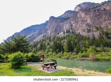 Beautiful picnic area by Seton lake in Lillooet, British Columbia, Canada. The view on the wooden picnic table surrounded by majestic mountains, green trees and turquoise lake. 