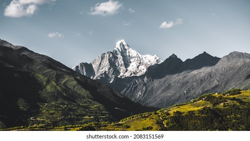 Beautiful picturesque landscape of snowy mountain peak over grasslands in Sichuan, China. One of Four sisters mountains in Tibetan mountain system. Bright day with clouds visible.