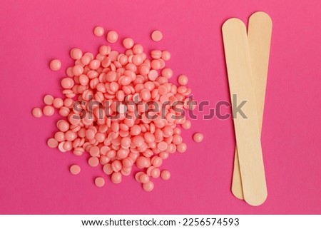 Beautiful pink depilatory wax granules and wooden spatulas on magenta background. Epilation, depilation, unwanted hair removal.