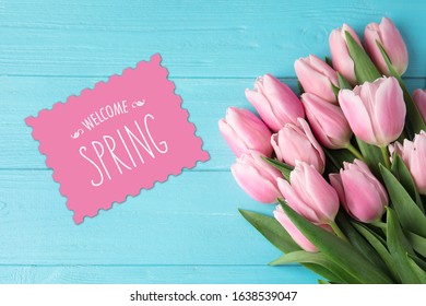 Beautiful pink tulips and greeting card on blue wooden background, top view. Hello spring