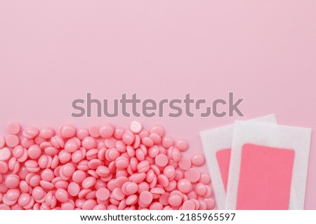 Beautiful pink wax granules and wax depilatory strips for delicate areas on a pink background. Place for text. Epilation, depilation, unwanted hair removal. Top view.