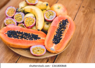 A beautiful plate of fresh sweet juicy tropical fruits - sliced papaya, passion fruits, bananas. A perfect healthy exotic fruit summer breakfast shot on wooden background. Flat lay close up view.