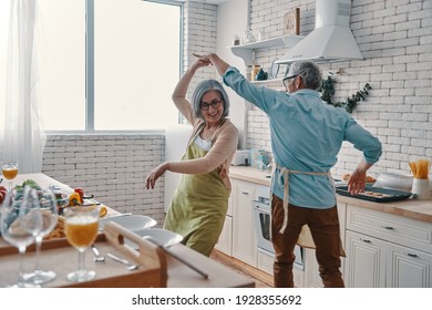 Beautiful playful senior couple in aprons dancing and smiling while preparing healthy dinner at home - Powered by Shutterstock