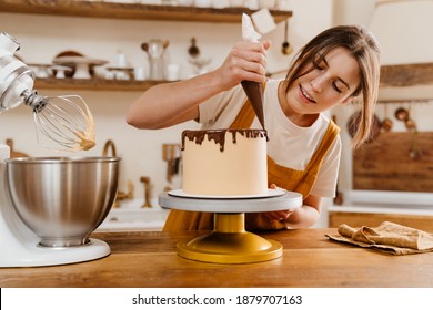 Hermosa cocinera repostera encantada haciendo tarta con crema de chocolate en la acogedora cocina