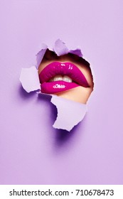 Beautiful plump bright lips of pink color peep into the slit of colored paper.make-up, makeup, advertising, facial, boutique, smooth skin, emotions, surprise.
