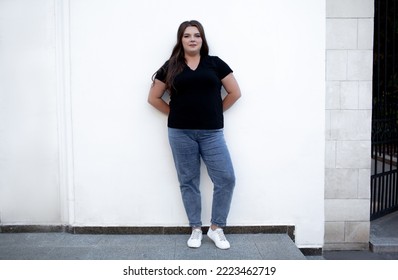 Beautiful plump woman wearing jeans and t-shirt posing against the street wall in the city