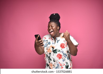 beautiful plus size black woman feeling excited and happy while holding and looking at her phone