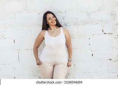 Beautiful plus size female model dressed in blank white shirt posing over brick wall background