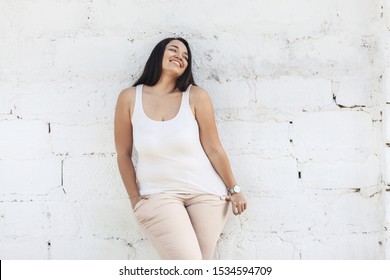 Beautiful plus size female model dressed in blank white shirt posing over brick wall background