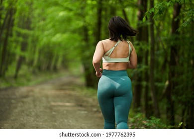 Beautiful plus size runner woman running on a dirt road in the forest