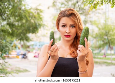Beautiful plus size woman comparing mens penis sizes using cucumber as an example. Summer hot portrait outdoor. Copy space