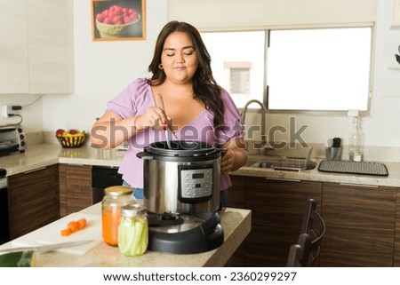 Beautiful plus size woman preparing food lunch in the pressure cooker or slow cooking pot and smiling looking happy doing housework in the kitchen