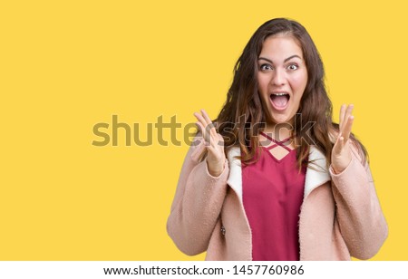 Beautiful plus size young woman wearing winter coat over isolated background celebrating crazy and amazed for success with arms raised and open eyes screaming excited. Winner concept