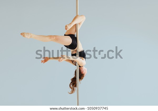 Beautiful pole\
dancer performing in the studio. Seria photo of middle aged red\
hair woman in black bra and shorts workout pole dance on air with\
different poses. Gray\
background.