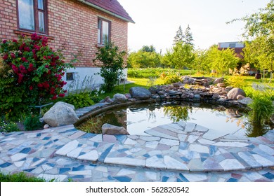 Beautiful Pond In A Backyard Of A Red Brick Home Surrounded With Stone During Summer