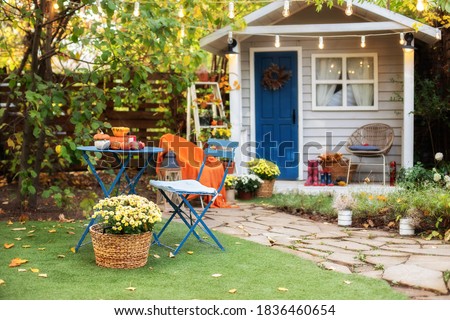 Beautiful porch home with autumn decorations on thanksgiving. 
 Garden table and chairs with apples and pumpkins on autumn yard. Terrace with retro light bulbs garlands. halloween. Interior cozy patio
