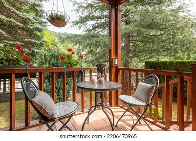 Beautiful Porch With Table And Two Chairs. Cozy House With Many Plants And Trees On Sunny Day In European Village.