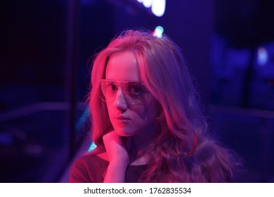 Beautiful portrait of girl in glasses near a red and blue neon sign in a cafe.