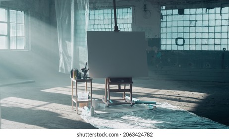 Beautiful Portrait Of An Isolated White Canvas Standing In The Middle Of An Empty Old Warehouse Building With Big Windows, Sun Shining Through Them. 