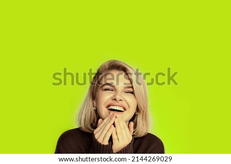 Beautiful portrait of a laughing blonde girl with a yellow green background, emotionally reacting to a joke