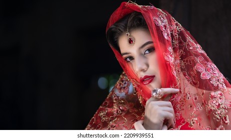 Beautiful Portrait Pretty Woman Red Dressed As An Indian Sexy Girl With Red Lips. Young Hindu Pakistani Bride And Glamour Makeup In A Fashion Jewelry Set. Traditional Indian Red Sari Clothing.