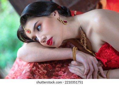 Beautiful Portrait Pretty Woman Red Dressed As An Indian Sexy Girl With Red Lips. Young Hindu Pakistani Bride And Glamour Makeup In A Fashion Jewelry Set. Traditional Indian Red Sari Clothing.