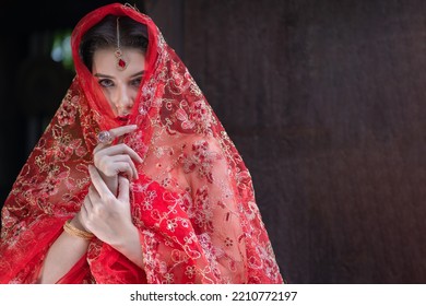 Beautiful Portrait Pretty Woman Red Dressed As An Indian Sexy Girl With Red Lips. Young Hindu Pakistani Bride And Glamour Makeup In A Fashion Jewelry Set. Traditional Indian Red Sari Clothing.