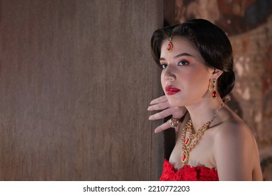 Beautiful Portrait Pretty Woman Red Dressed As An Indian Sexy Girl With Red Lips. Young Hindu Pakistani Bride And Glamour Makeup In A Fashion Jewelry Set. Traditional Indian Red Sari Clothing.