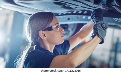 Beautiful Portrait of a Professional Female Car Mechanic is Working Under a Vehicle on a Lift in Service. She is Using a Ratchet. Specialist is Wearing Safety Glasses. Modern Clean Workshop. - Powered by Shutterstock