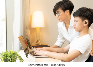 Beautiful Portrait Of A Smart Look Asian Mother Advice Her Teenager Son While Using Computer Laptop To Studying Online During Covid-19 Pandemic Lockdown. New Normal, Homeschool, Home Based Learning.