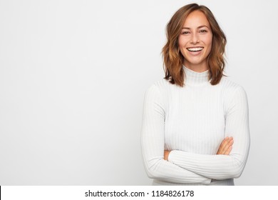 Beautiful Portrait Of Smiling Young Adult And Woman Looking In Camera, Standing With Arms Crossed And Giving A Beautiful Smile With White Teeth, Isolated On White 
