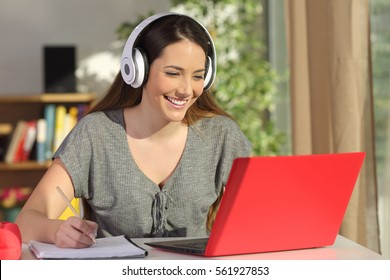 Beautiful portrait of a student learning on line watching video tutorials with a red laptop and headphones in a table at home