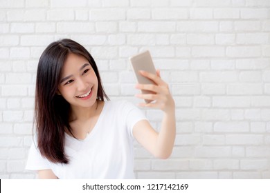 Beautiful Portrait Young Asian Woman Taking A Selfie With Smart Mobile Phone On Concrete Cement White Background, Girl Is Photographing With Happy And Smile With Fun, Lifestyle Concept.