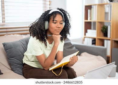 A beautiful, positive young Black female college student studying online at home, wearing headphones, studying online on her laptop computer. education and wireless technology concepts - Powered by Shutterstock