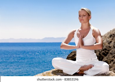 Beautiful positiveblond girl clothing in white sit at the seaside on the rock and meditating in yoga pose - Powered by Shutterstock