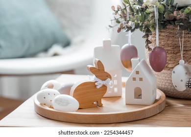 A beautiful postcard. The concept of the Bright Easter holiday. Flowers, rabbits, Easter eggs and Scandinavian white houses on a wooden table in a cozy living room. - Powered by Shutterstock