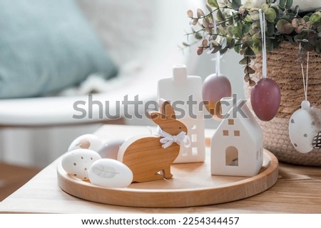 A beautiful postcard. The concept of the Bright Easter holiday. Flowers, rabbits, Easter eggs and Scandinavian white houses on a wooden table in a cozy living room.
