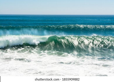 A beautiful and powerful turquoise wave in high winds curls while white spray mist forms and at its crest in Huntington Beach.
