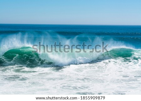 A beautiful and powerful turquoise wave in high winds curls while white spray mist forms and at its crest in Huntington Beach.